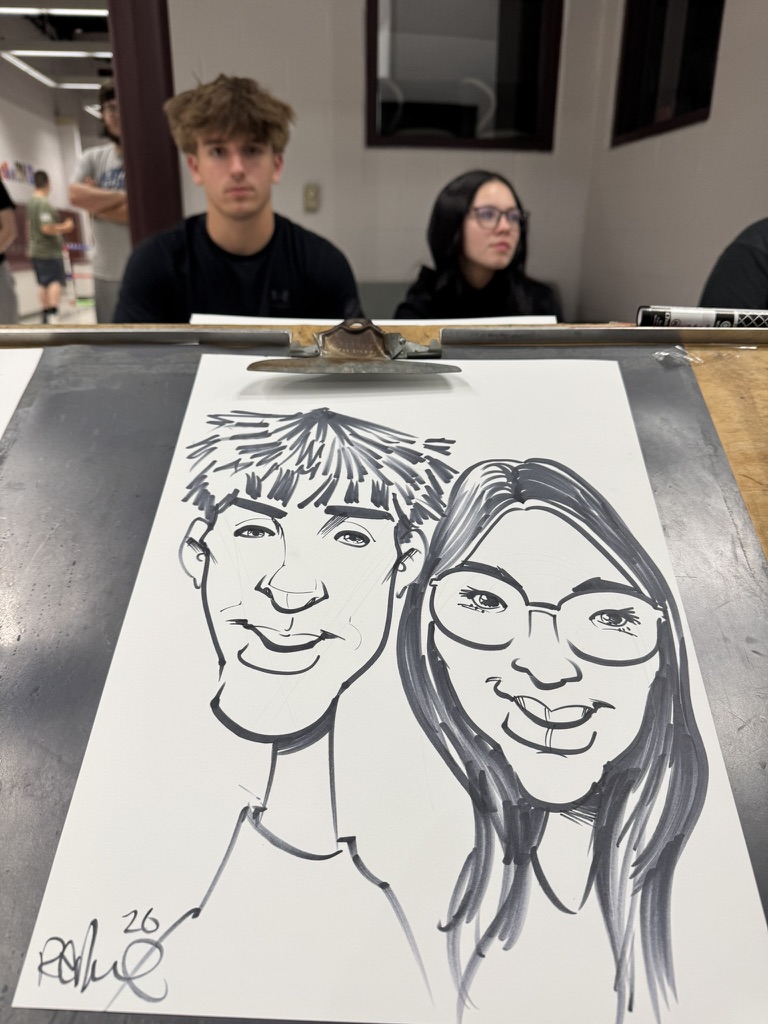 A finished black-and-white caricature on a drawing table with two guests nearby