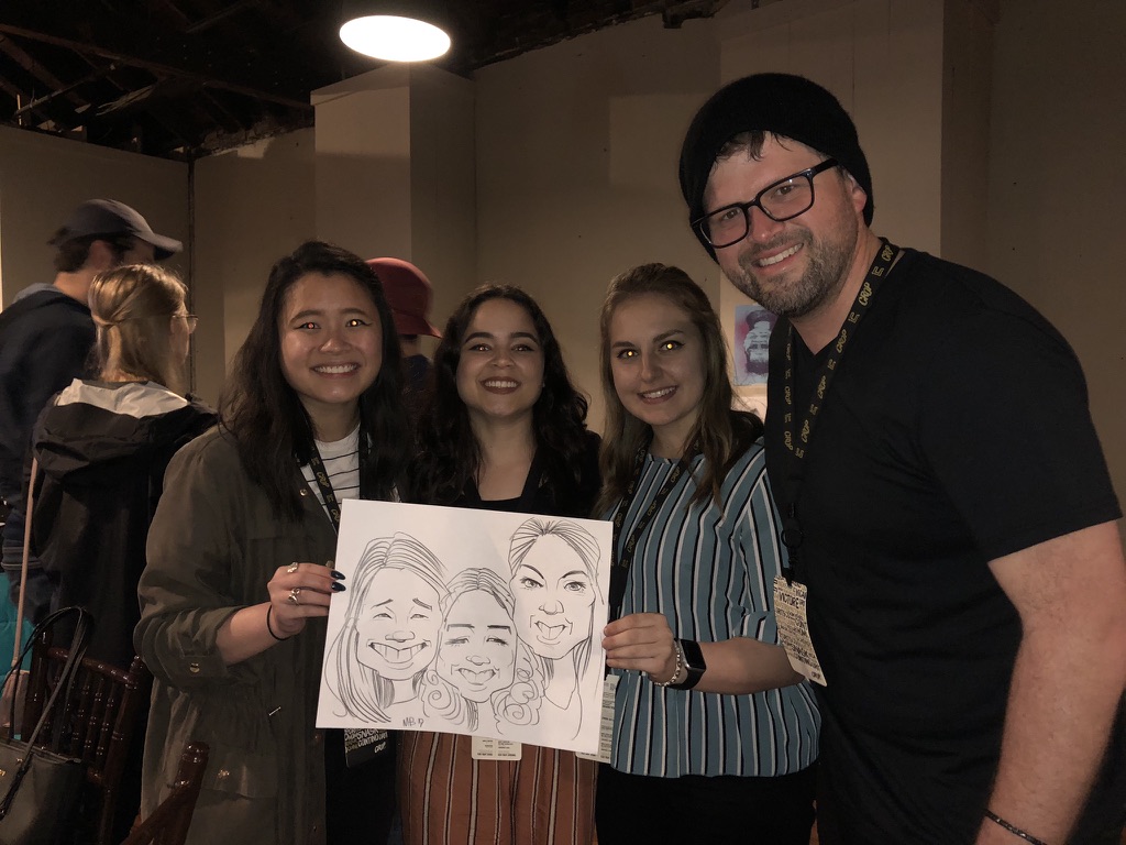 Four attendees at an indoor event hold a live group caricature